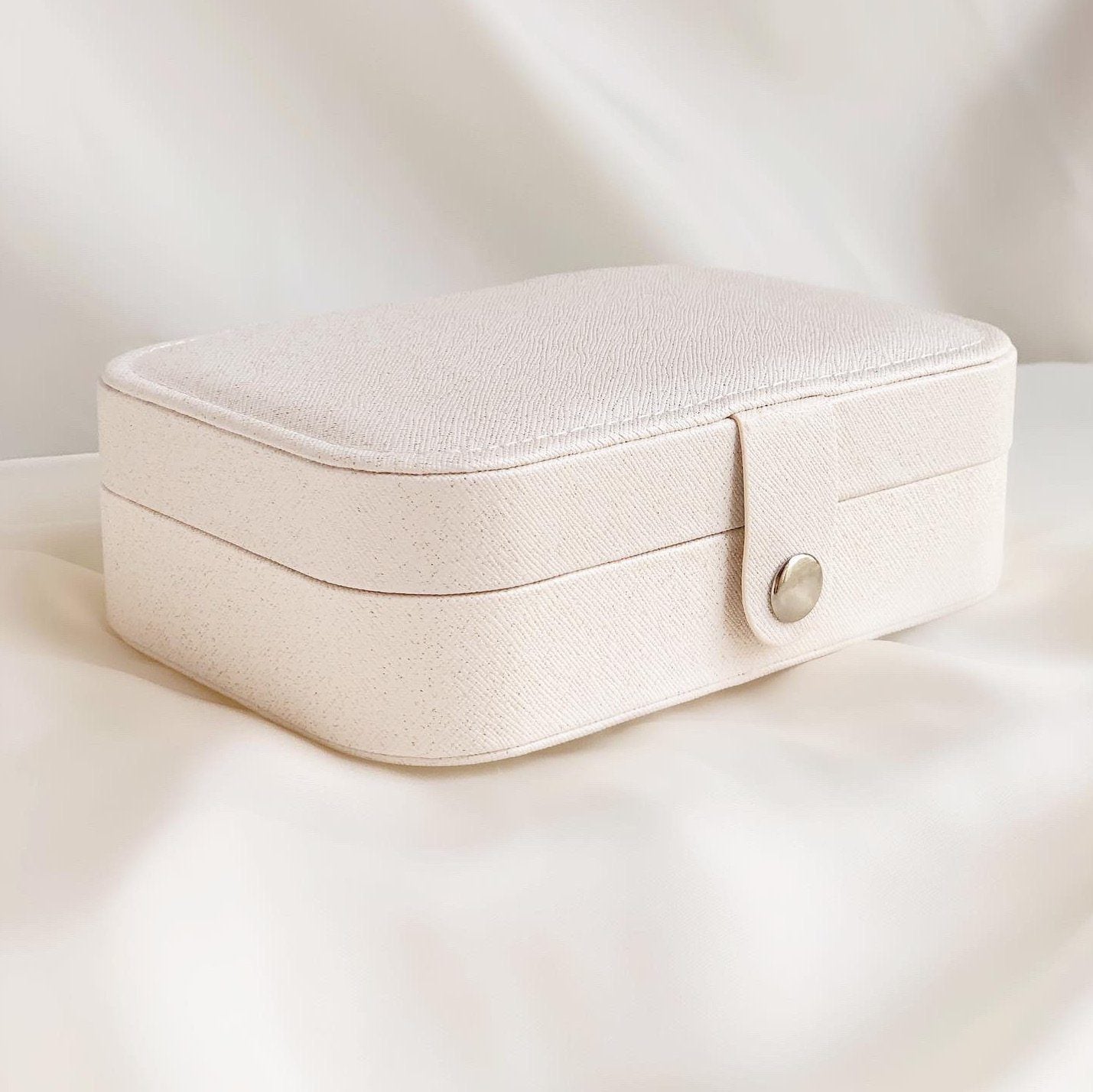 White jewelry carrying case sitting on a white piece of satin.