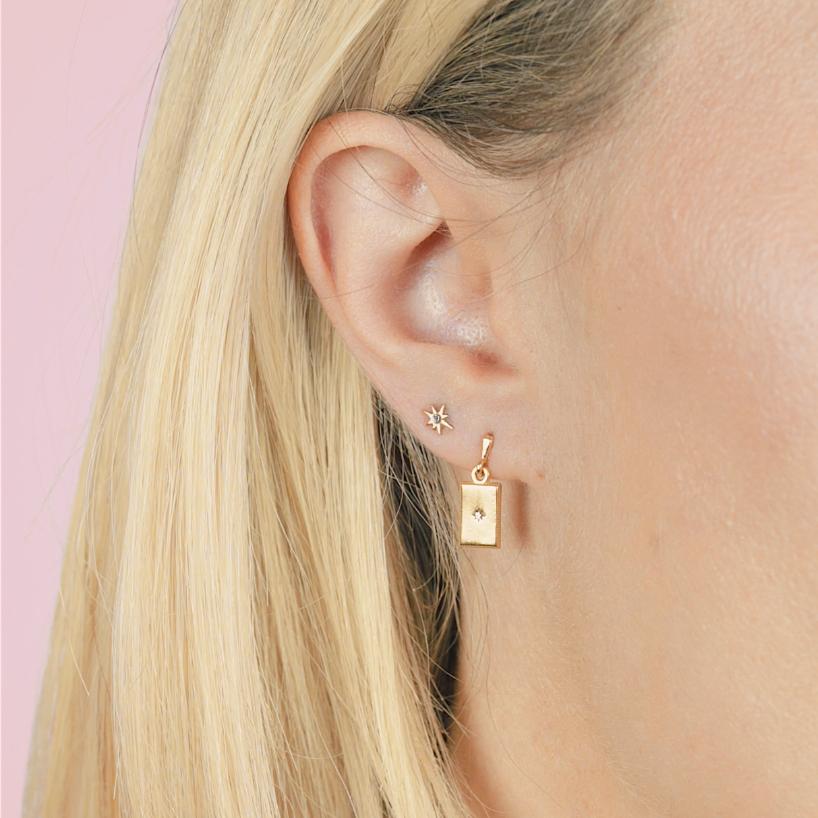Close up of a dainty star earring and rectangle earring on a models ear.