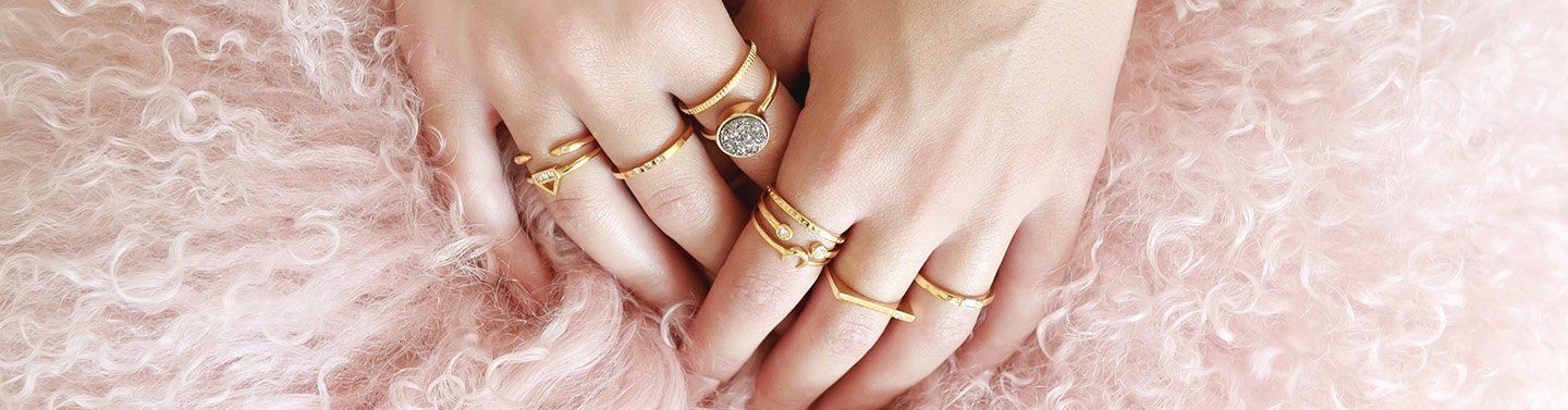 image of two hands on a pink fluffy pillow with dainty gold rings on each finger.