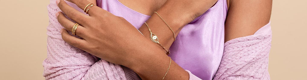 Image showing the upper body of a model with her arms crossed wearing dainty gold handmade bracelets and rings by Katie Dean Jewelry