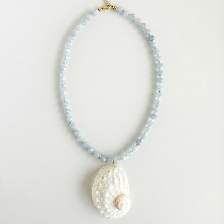 Necklace with light blue beads and a large white abalone shell pendant on a light gray background