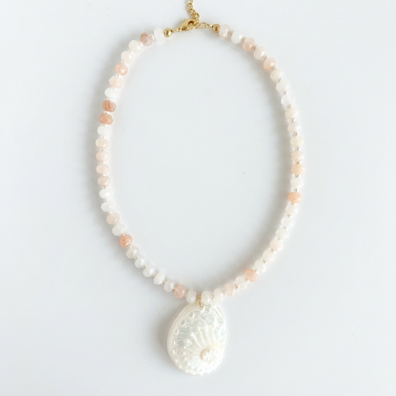 Necklace with light pink and white beads and a large white abalone shell pendant on a light gray background