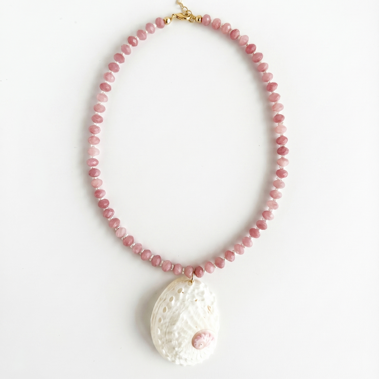 Necklace with pink beads and a large white abalone shell pendant on a white background