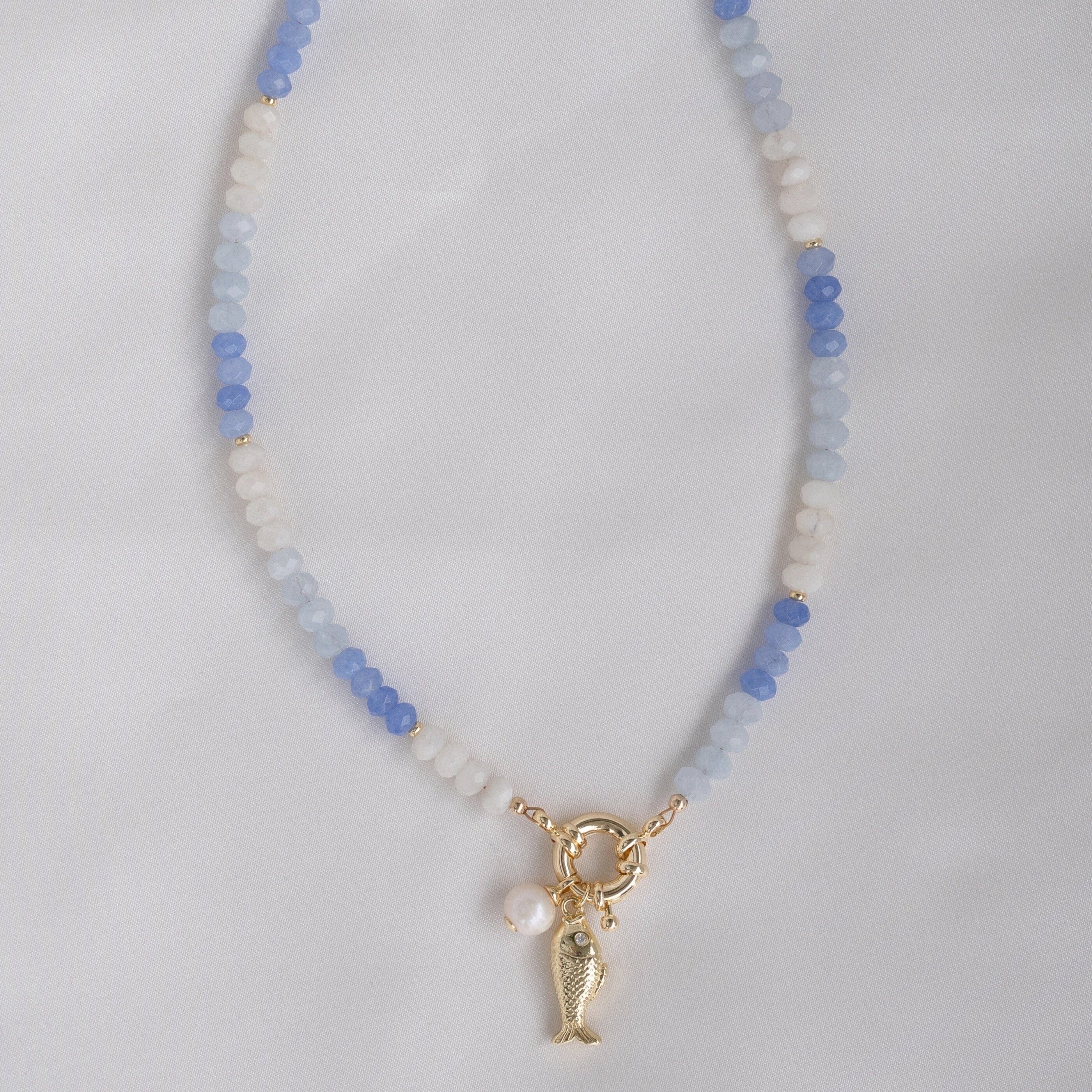Necklace with blue and white beads and a gold fish charm and freshwater pearl charm on a light gray background.