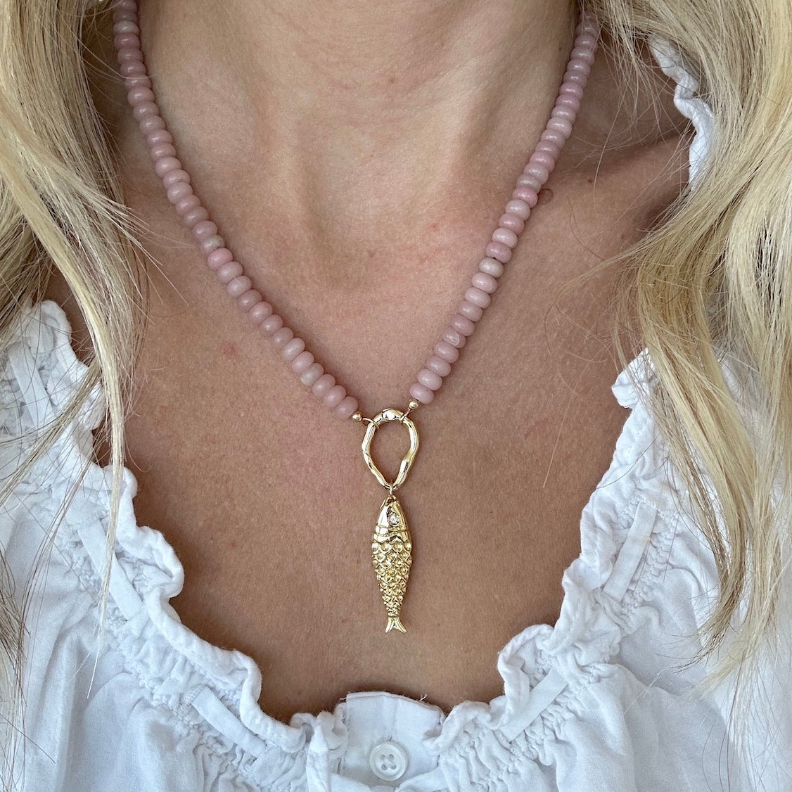 Pink opal beaded necklace with gold fish charm and gold carabiner clasp worn by a person in a white blouse, hand beaded by Katie Dean Jewelry.