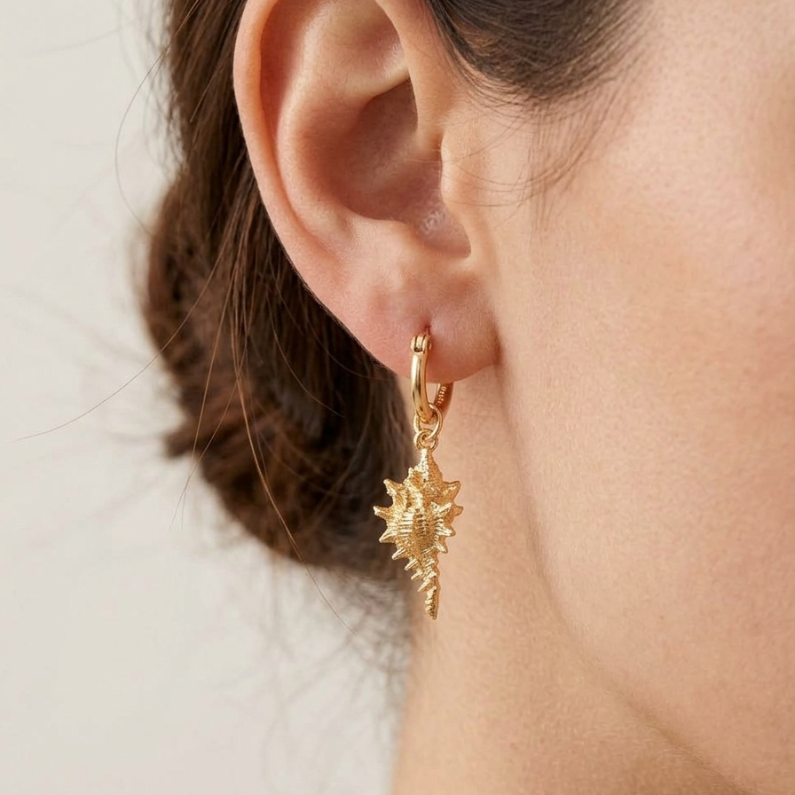 gold hoop earrings with detailed conch shell charms on a person