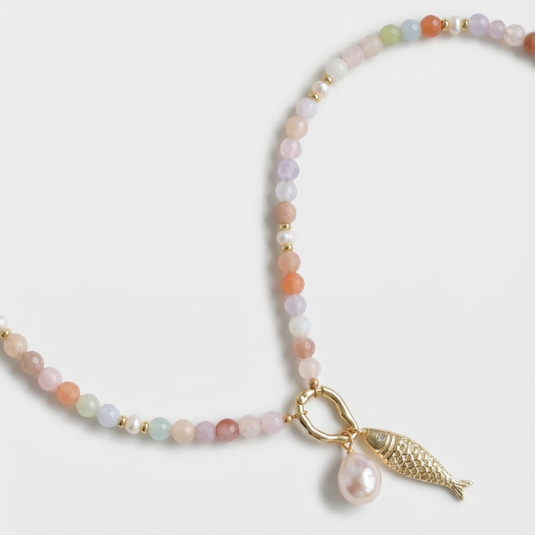Beaded necklace with a gold fish charm and pearl on a light gray background
