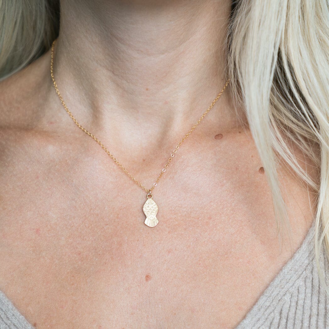 Gold necklace with a fish pendant on a person's neck