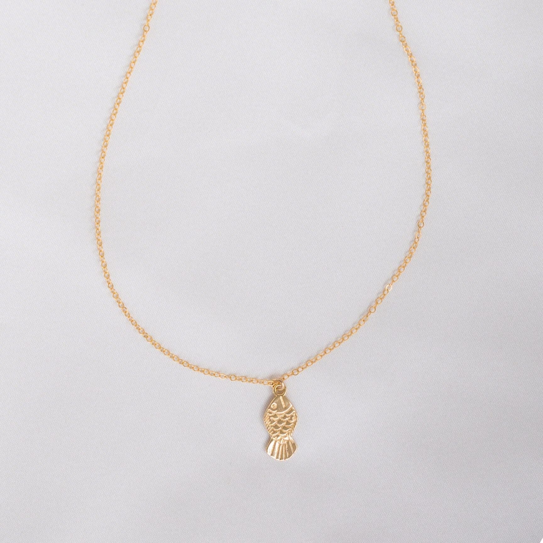 Gold necklace with a fish pendant on a light gray background