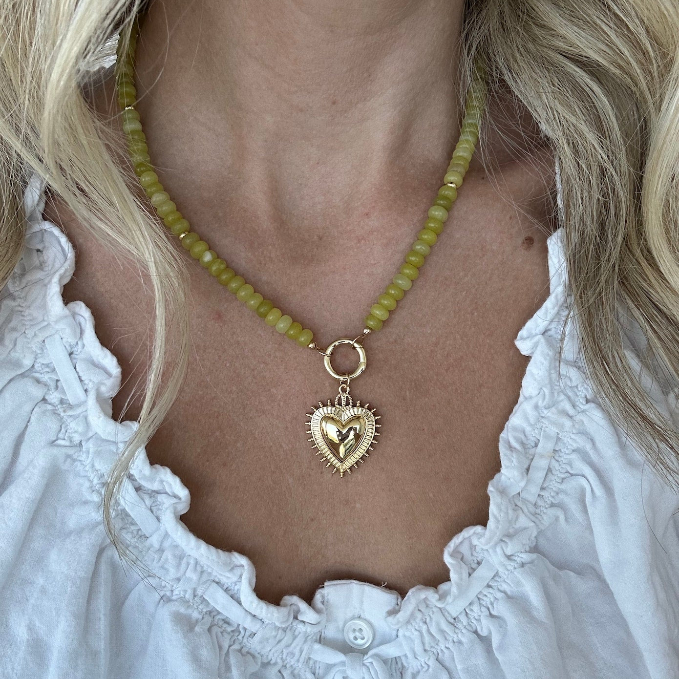 Green gemstone beaded necklace with gold fill heart charm and carabiner clasp worn by a woman in a white top.