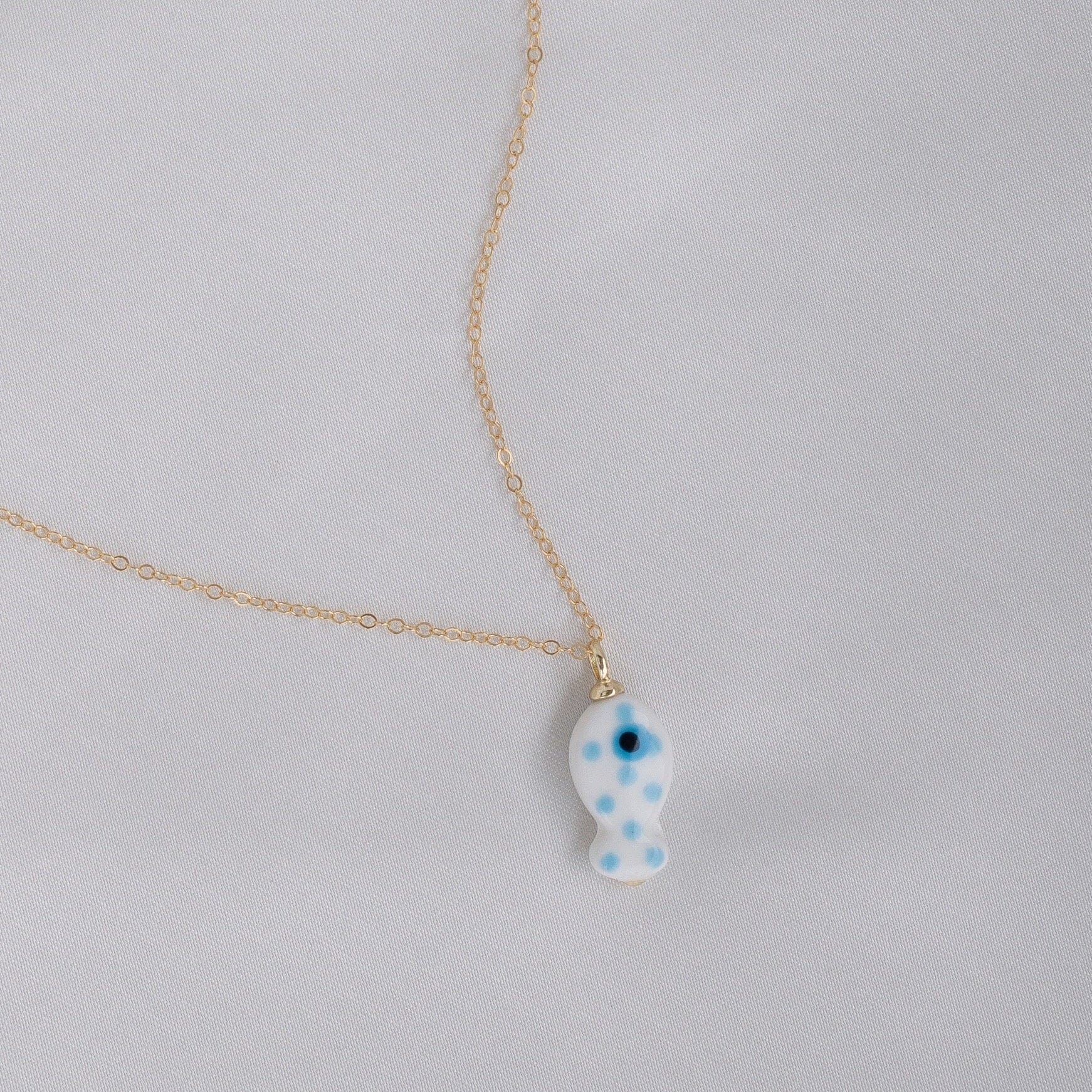 Gold chain necklace with blue ceramic fish charm with polka dots on white background.