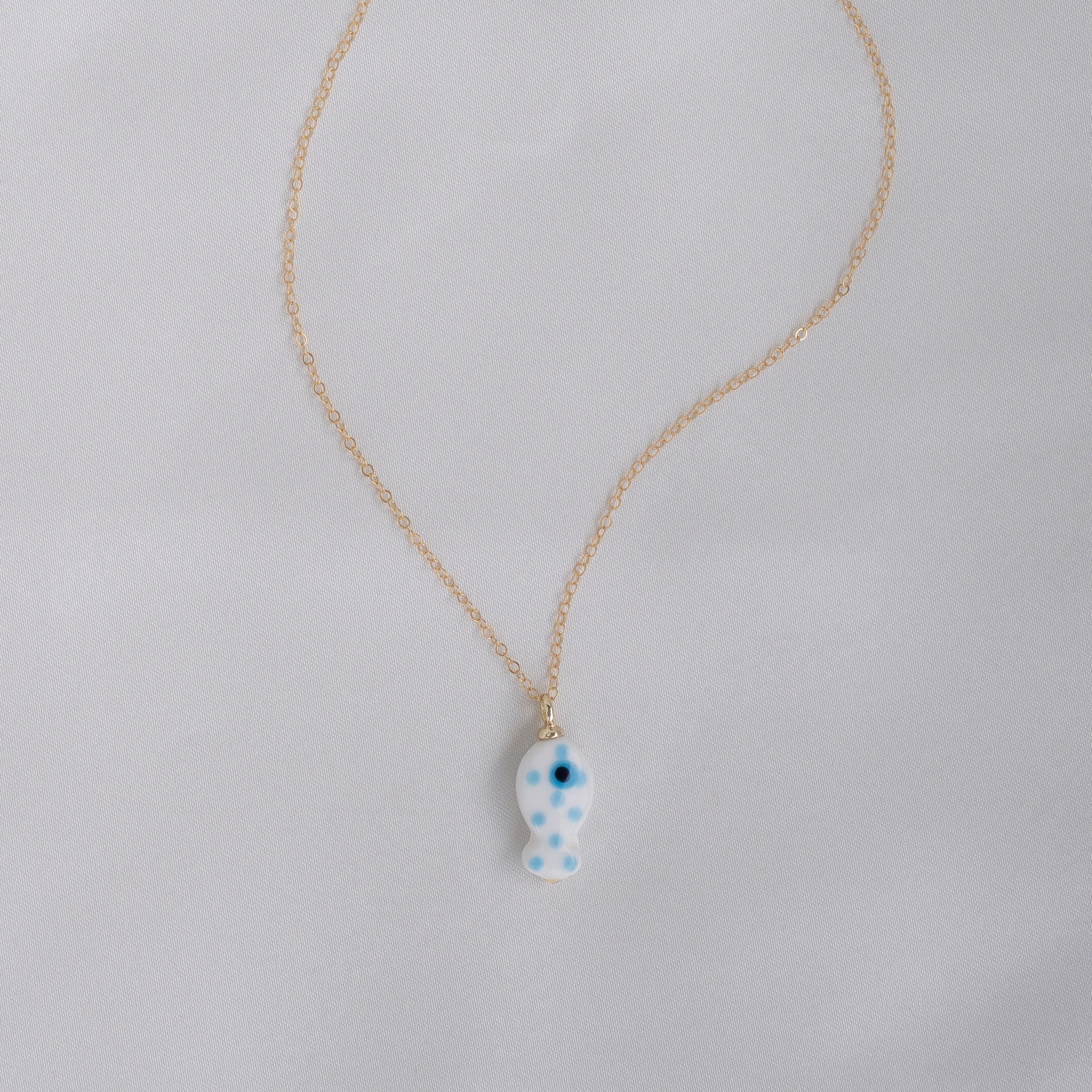 Gold chain necklace with blue ceramic fish charm with polka dots on white background.