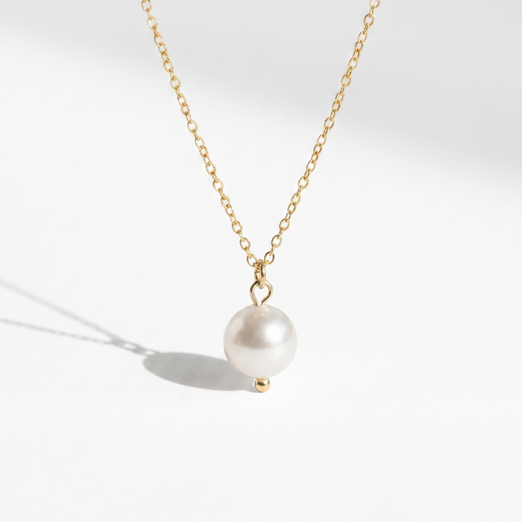 A delicate gold chain necklace featuring a single, lustrous white pearl pendant held in a small gold setting, photographed on a clean white background with a soft shadow.