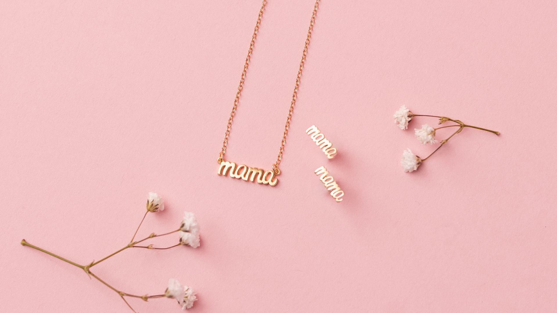 Dainty gold Mama Necklace and Mama Studs, made in America by Katie Dean Jewelry as seen on a pink background.