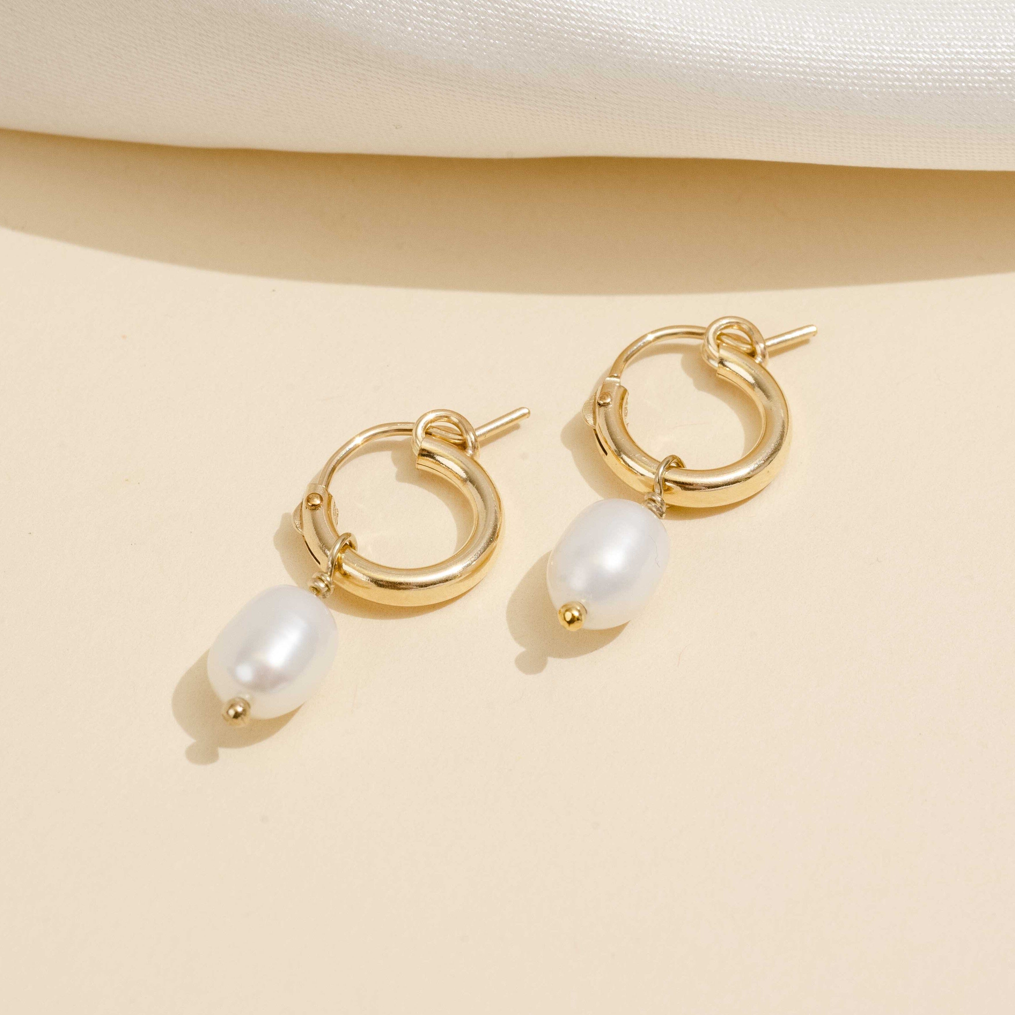 Dainty gold Pearl hoops by Katie Dean Jewelry as seen on a tan background.