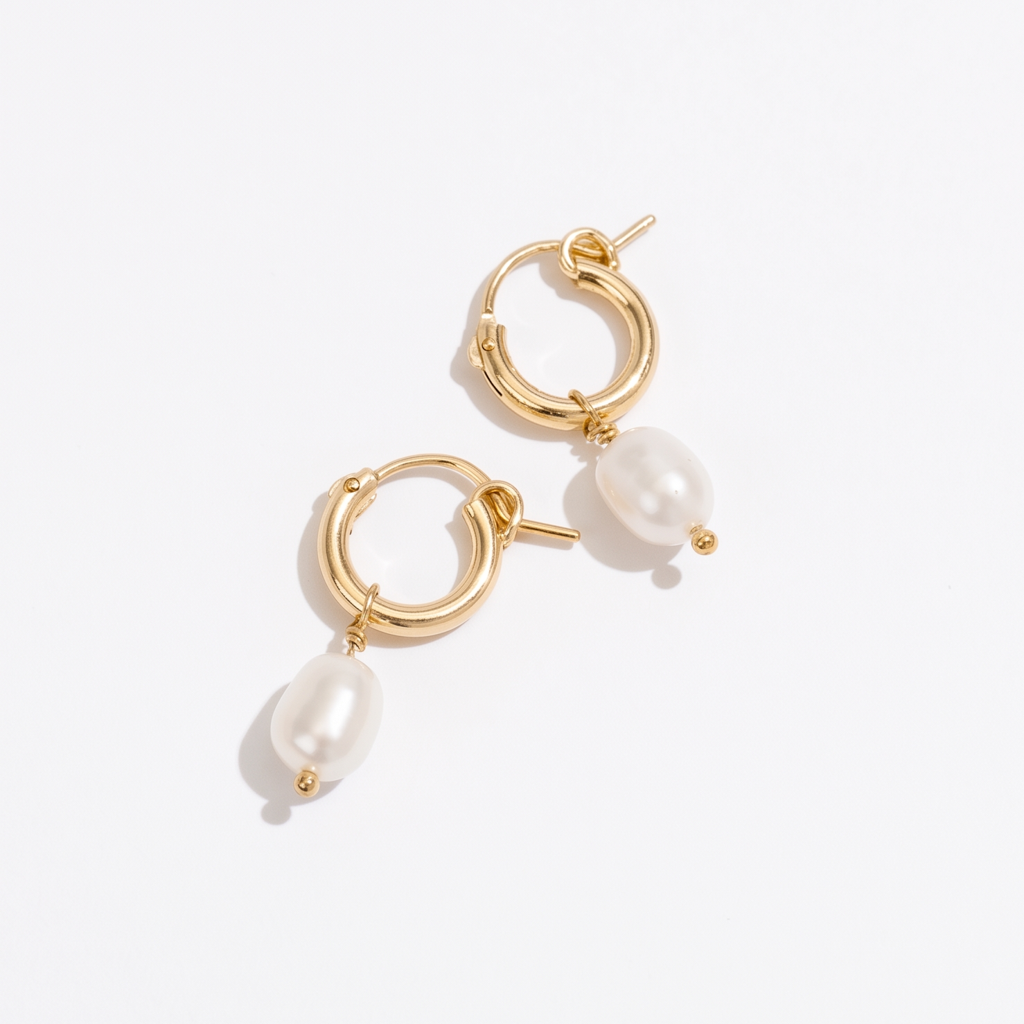 A pair of gold hoop earrings with dangling baroque pearl beads, photographed on a clean white background.