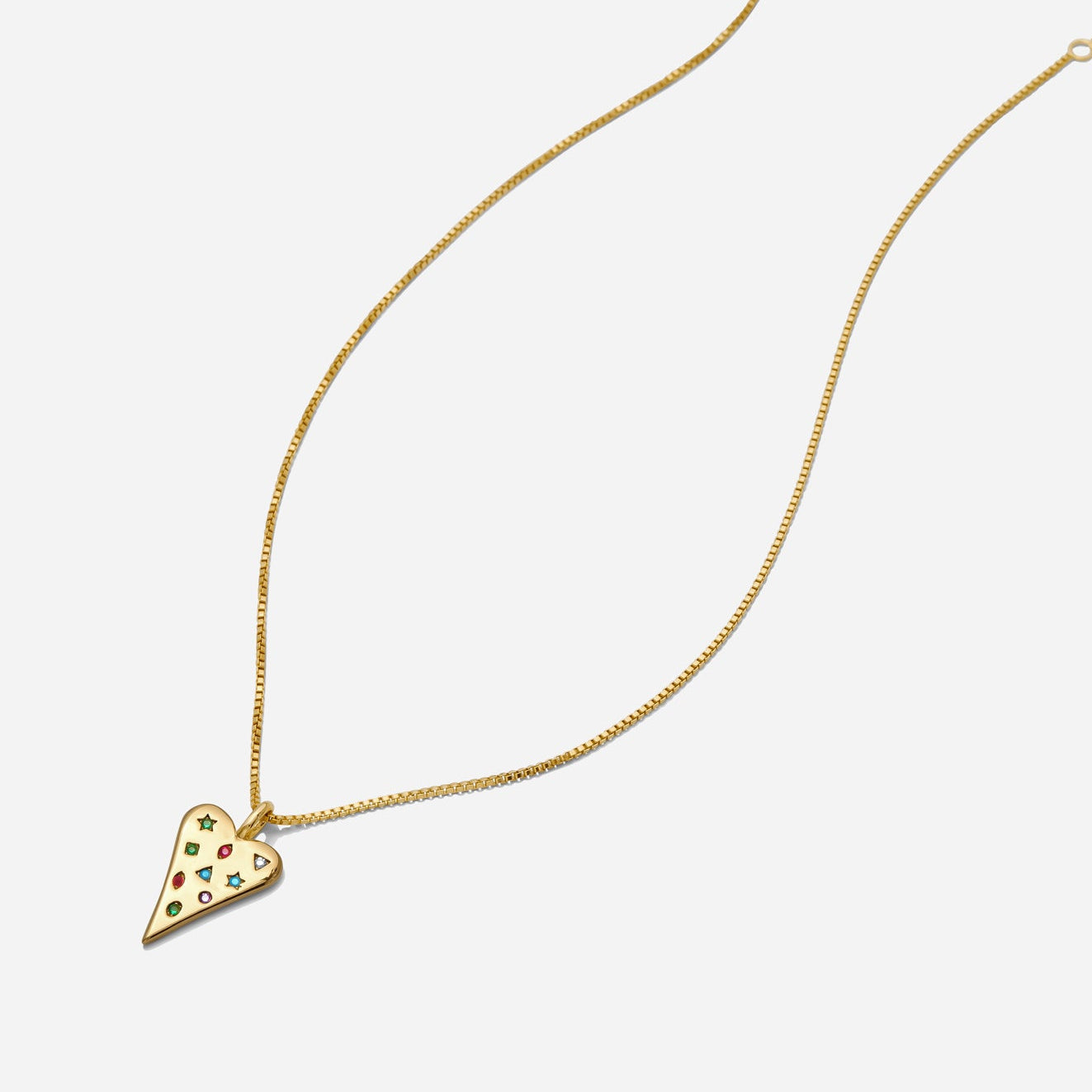 Dainty gold heart pendant necklace with multicolor gemstone accents on a delicate chain laying on a white background.