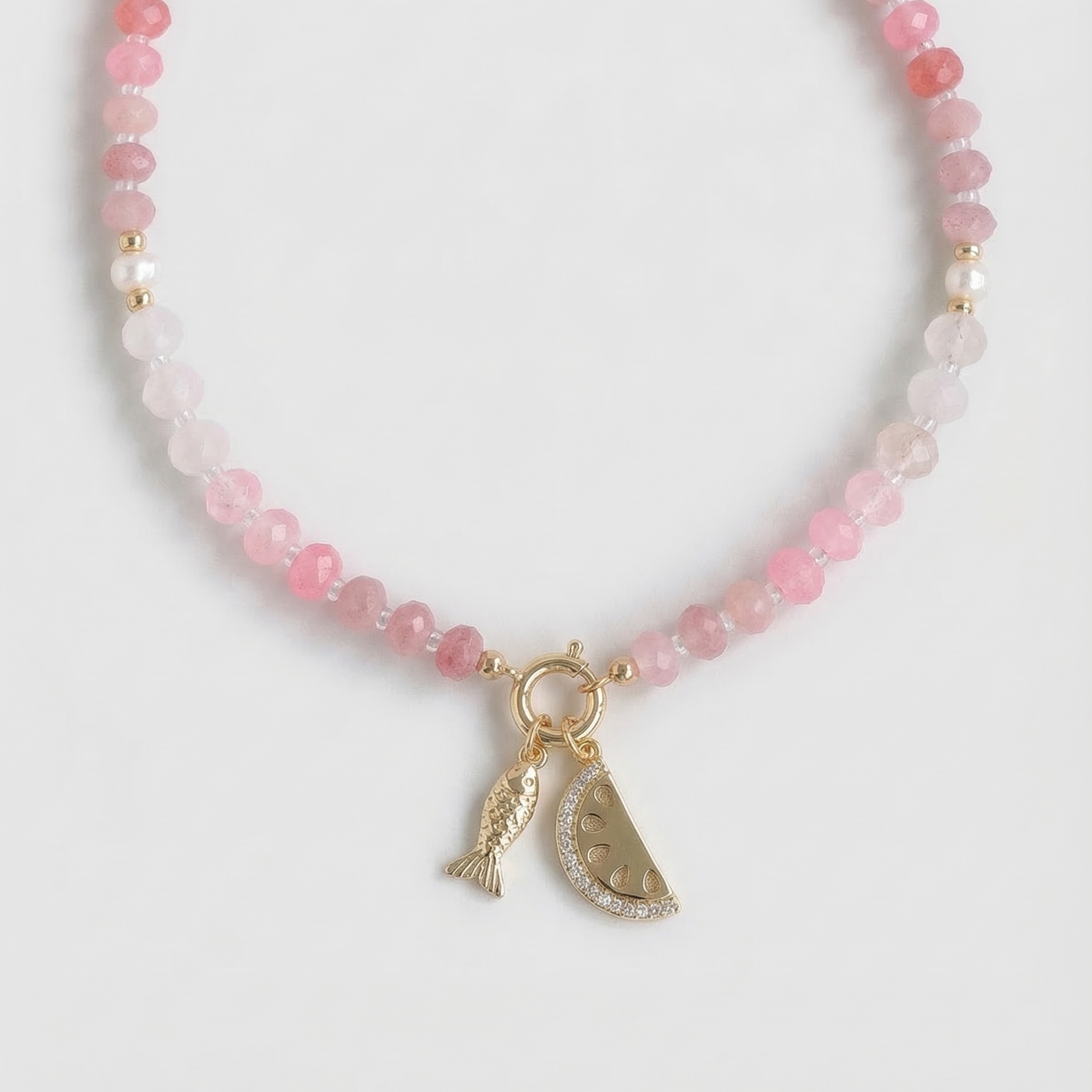 Necklace with pink beads and gold fish and watermelon charms on a white background