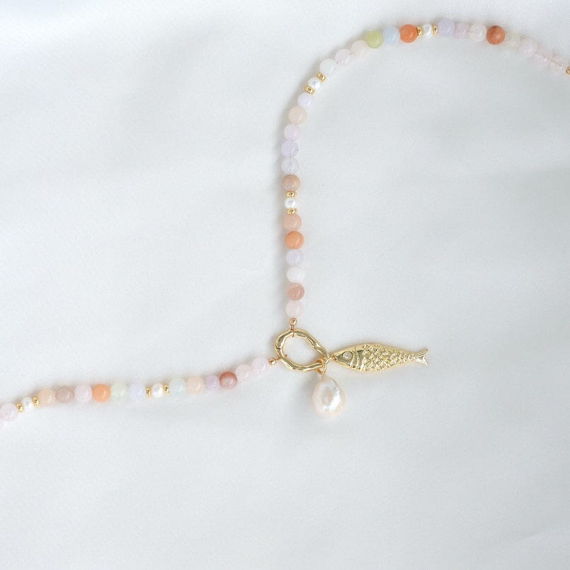Necklace with beads and a gold fish charm and baroque pearl charm on a white background