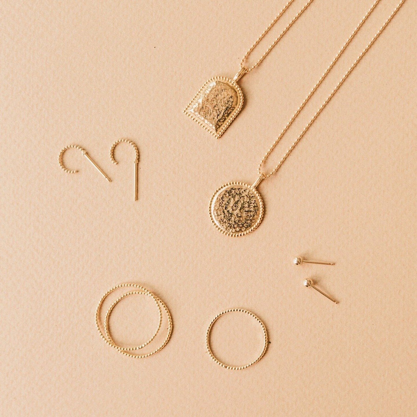 Beaded Coin Necklace, Beaded Arch Necklace, Beaded Rings and Beaded Hoop Earrings laying on a light brown background.