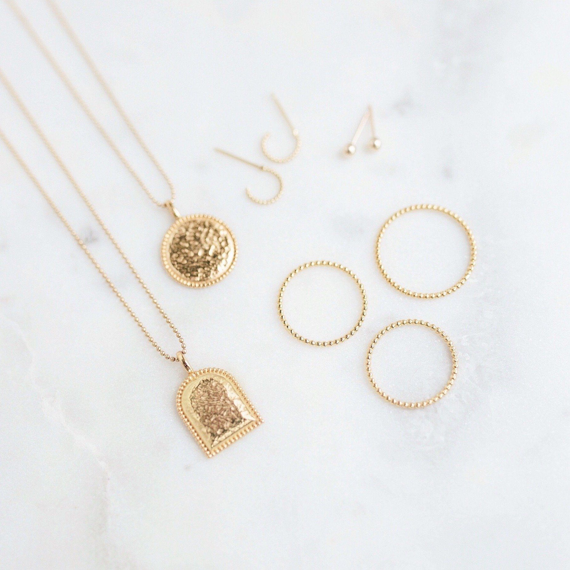 Beaded Coin Necklace, Beaded Arch Necklace, Beaded Rings and Beaded Hoop Earrings laying on a marble slab.