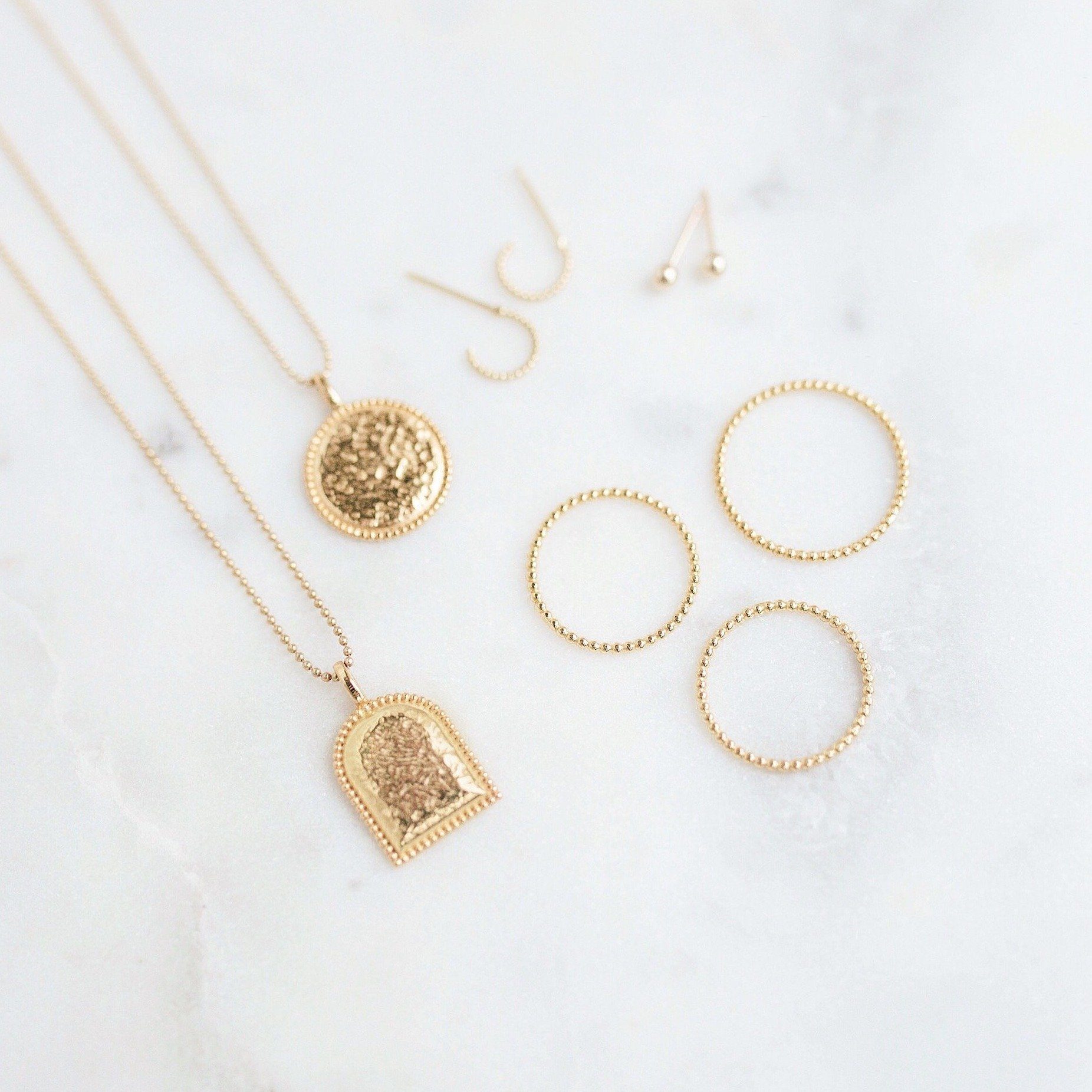 Beaded Coin Necklace, Beaded Arch Necklace, Beaded Rings and Beaded Hoop Earrings laying on a marble slab.