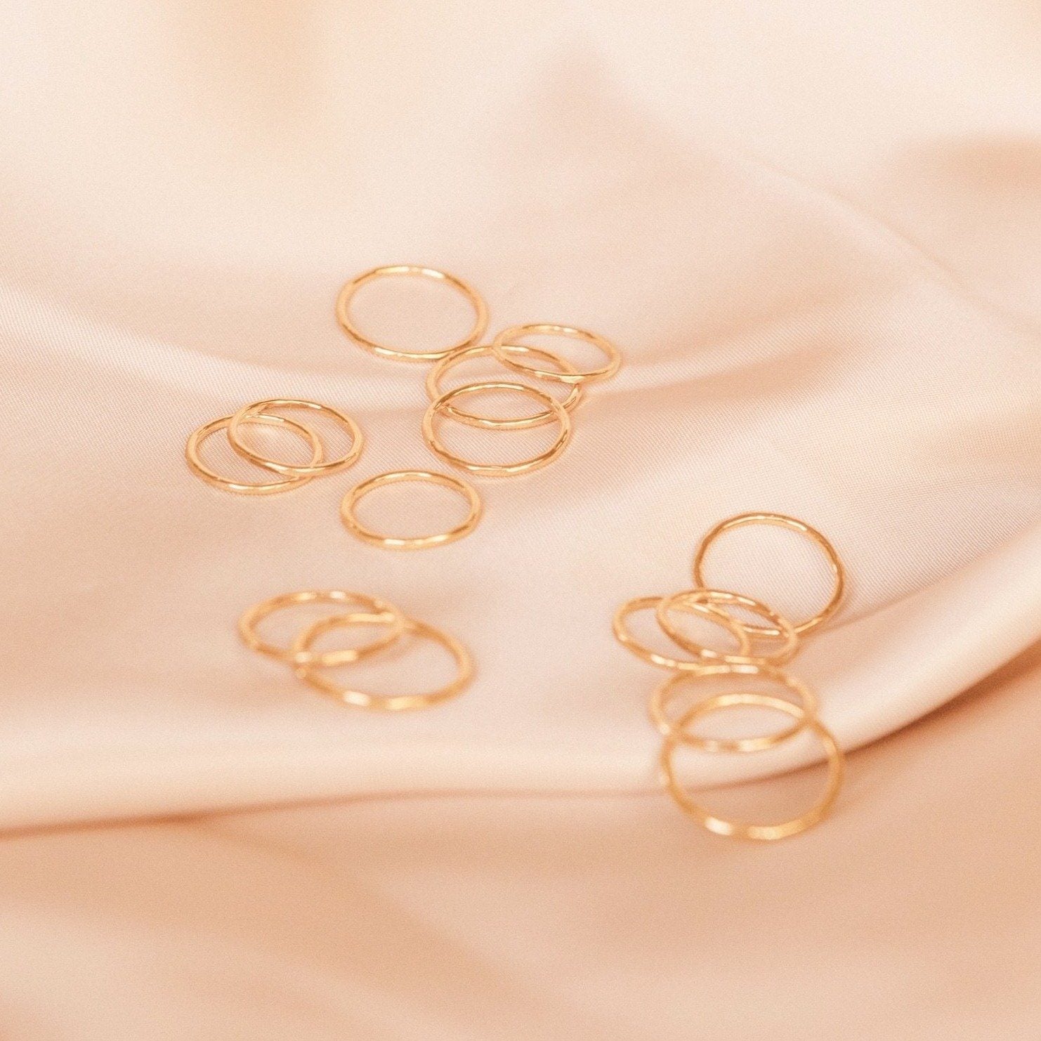 Dainty gold hammered band rings laid out on a piece of pink satin. Handmade by Katie Dean Jewelry in California.