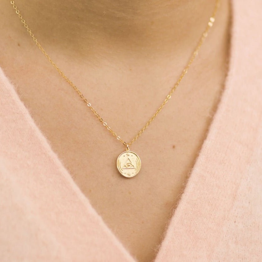 Model wearing a gold dainty necklace with round charm with an all seeing eye design, designed and made by Katie Dean Jewelry
