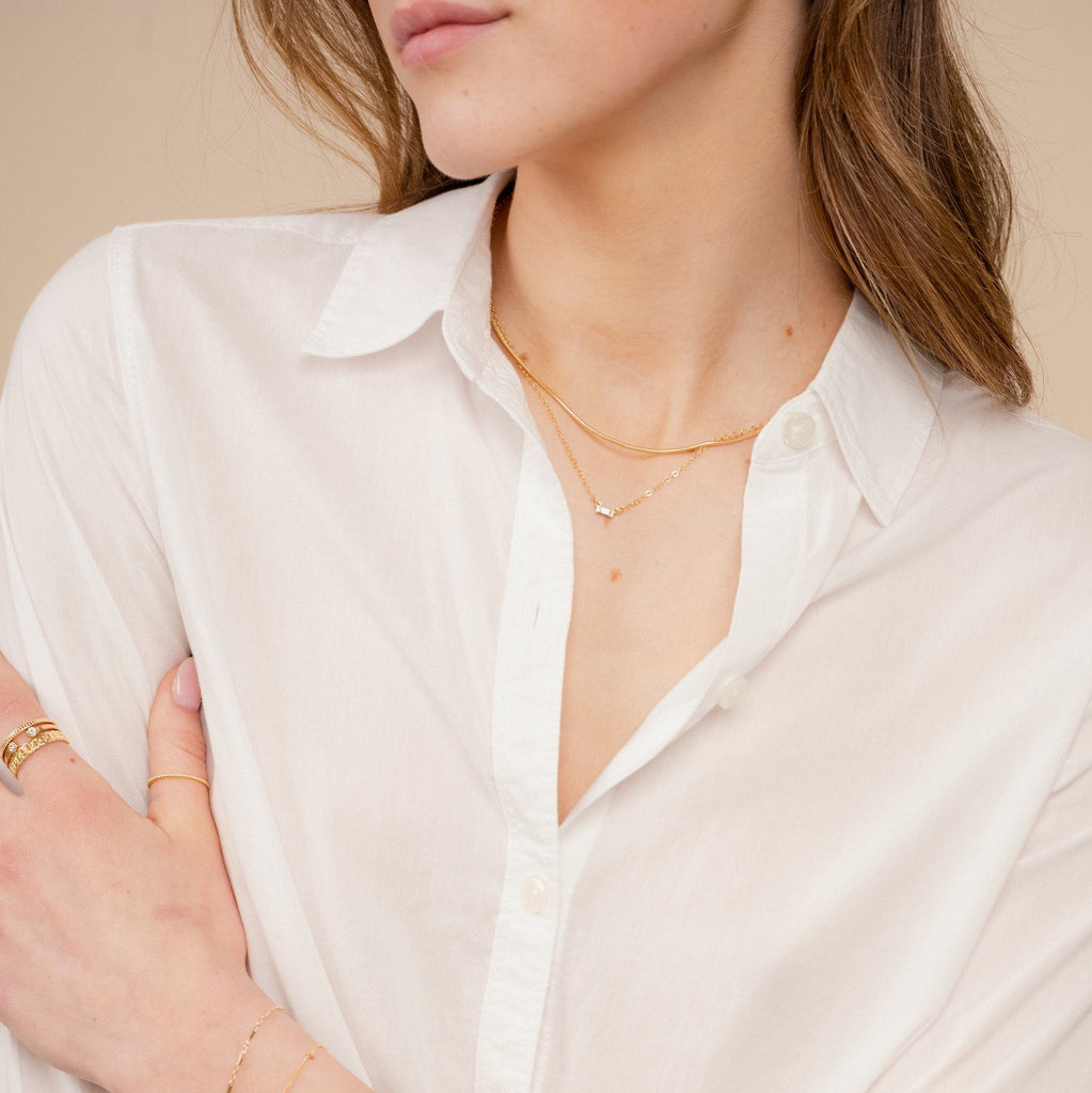 The dainty gold Elegant Necklace Set by Katie Dean Jewelry as seen on a model wearing a white button up collared shirt and dainty gold stacking rings.