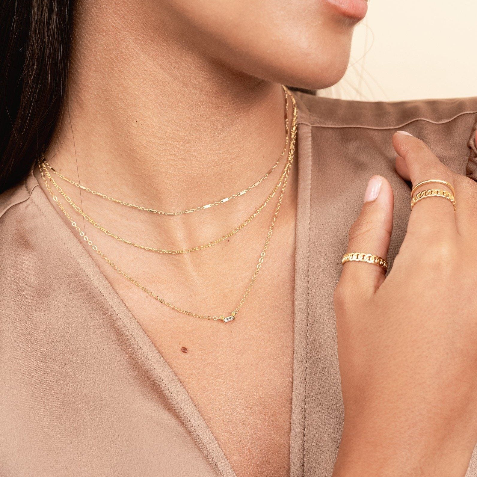 Model wearing brown silk top, looking to the side, wearing the gold Linked Choker, Figaro Chain Choker and Baguette Necklace. Handmade in California by Katie Dean Jewelry.