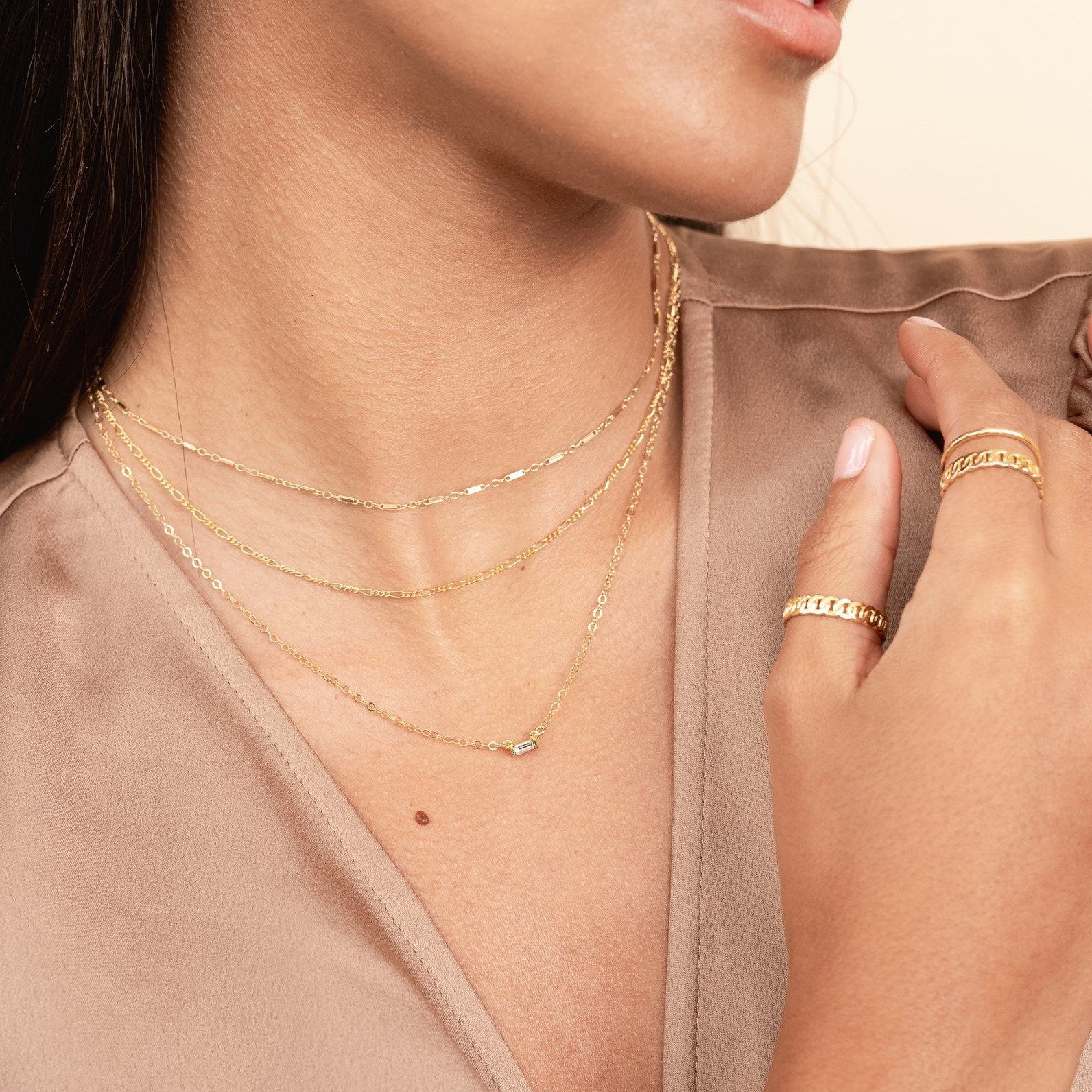 Model wearing brown silk top, looking to the side, wearing the gold Linked Choker, Figaro Chain Choker and Baguette Necklace. Handmade in California by Katie Dean Jewelry.