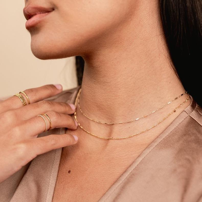 Model wearing brown silk top, looking to the side, wearing the gold Linked Choker and Figaro Chain Choker. Handmade in California by Katie Dean Jewelry.