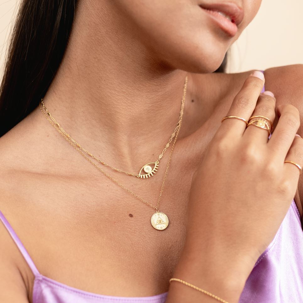 Picture of a model showing her upper body and wearing two dainty gold necklaces, one Evil Eye Necklace and the All Seeing Eye Necklace handmade by Katie Dean Jewelry