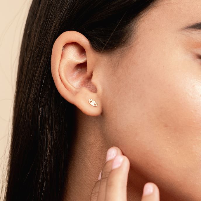 Picture of a model showing her ear with a dainty gold evil eye stud earring, made by Katie Dean Jewelry.