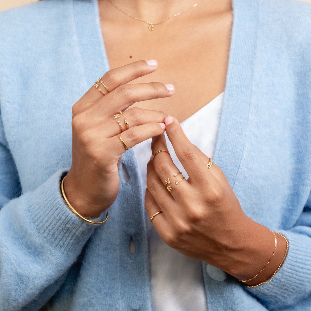 Two hands showing in the center of the image wearing the Initial Rings and Hammered Band Rings made by Katie Dean Jewelry.