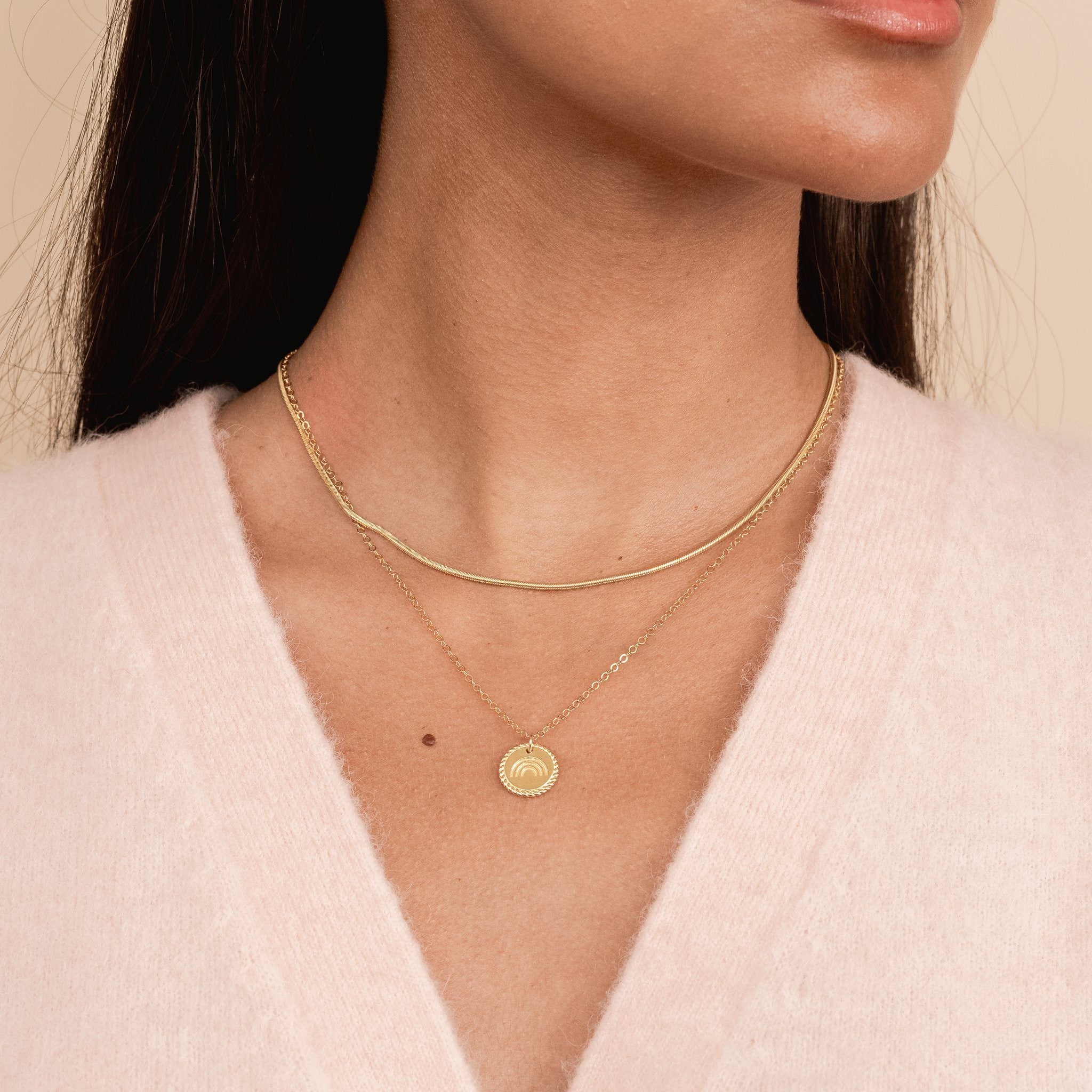 Model wearing a pink cardigan sweater while wearing a gold Snake Chain Necklace layered with the dainty gold Rainbow Necklace by Katie Dean Jewelry.