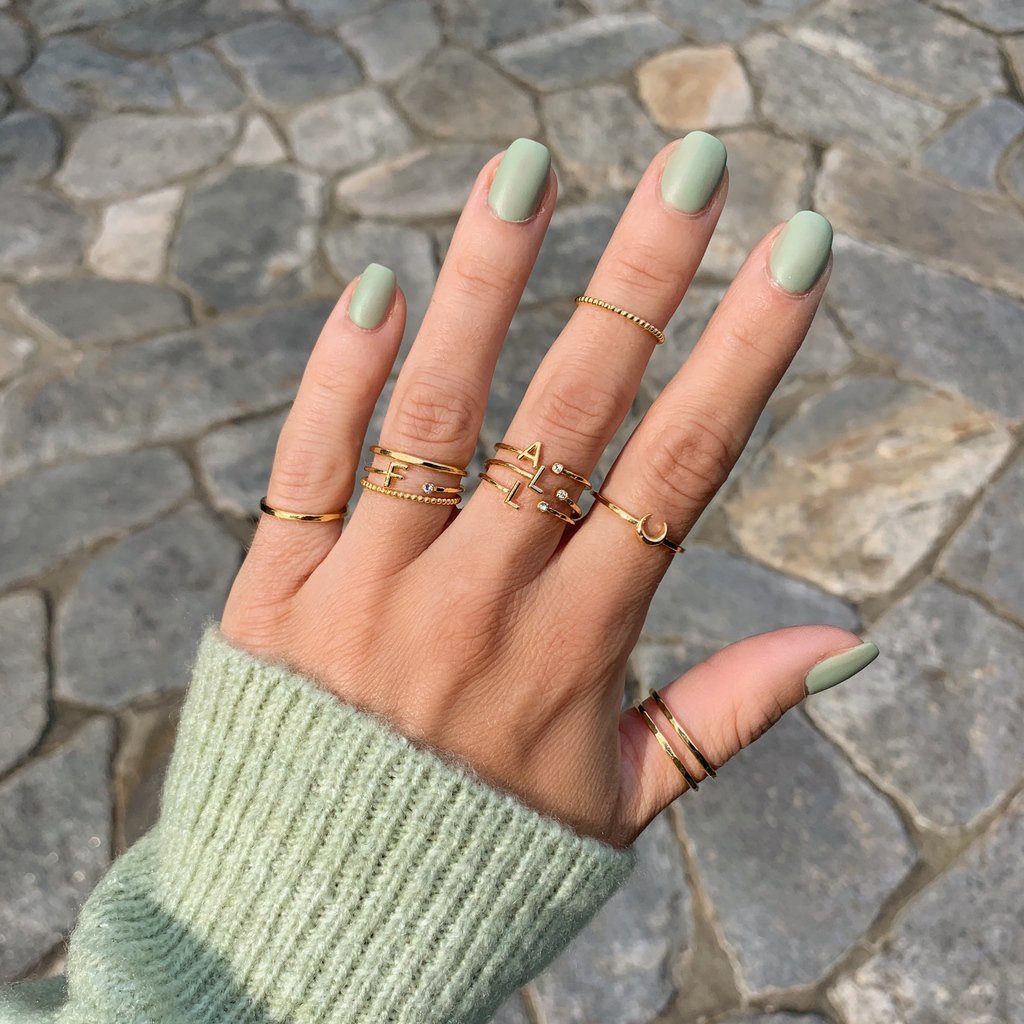 Picture of a hand showing the sleeve of a light green sweater and the nails on the hand are painted with green essie polish and on each finger Katie Dean Jewelry Initial Rings, Beaded Ring, Moon Ring and Hammered Band Rings