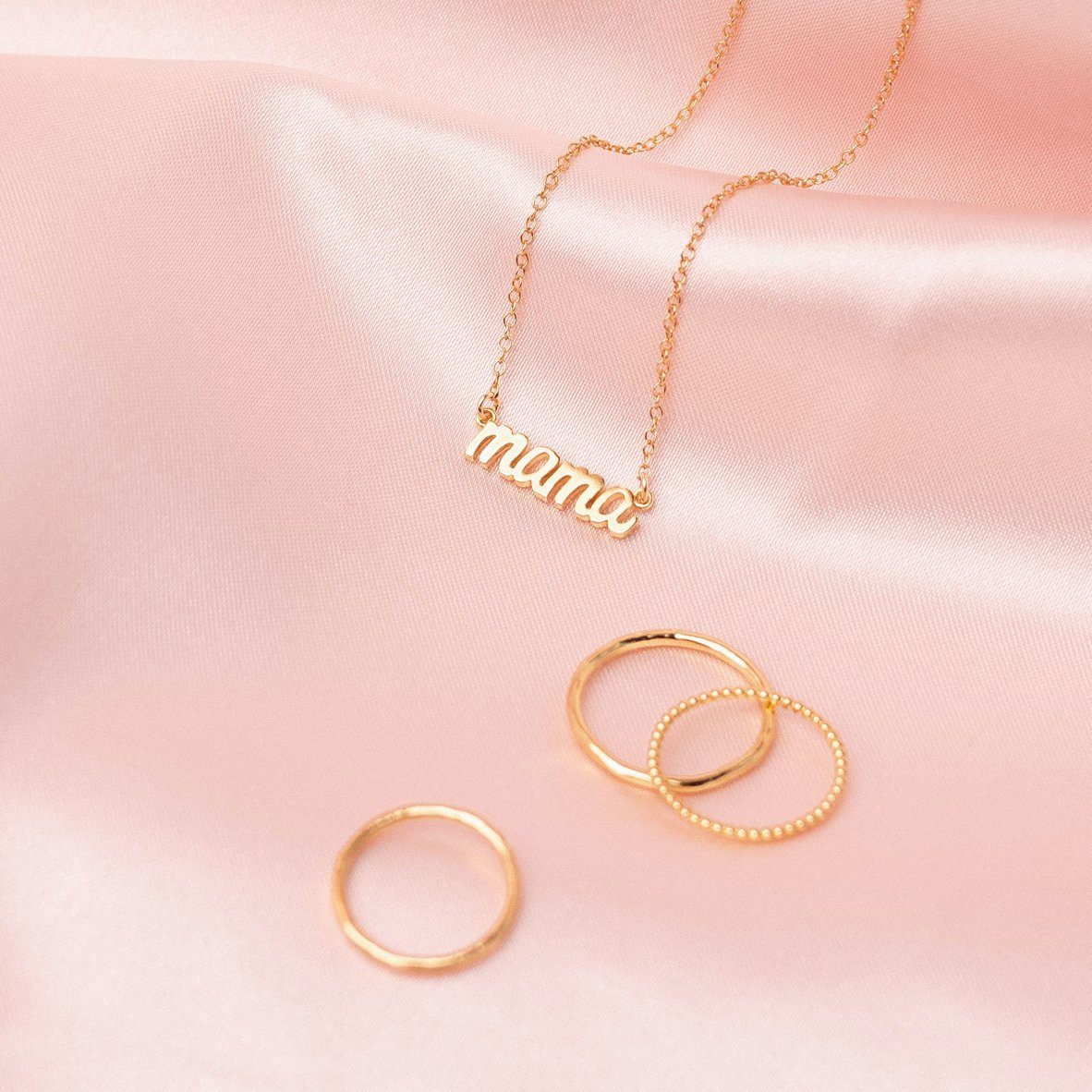 Dainty gold Mama Necklace perfect for Mother's Day as seen on a piece of pink satin, made by Katie Dean Jewelry