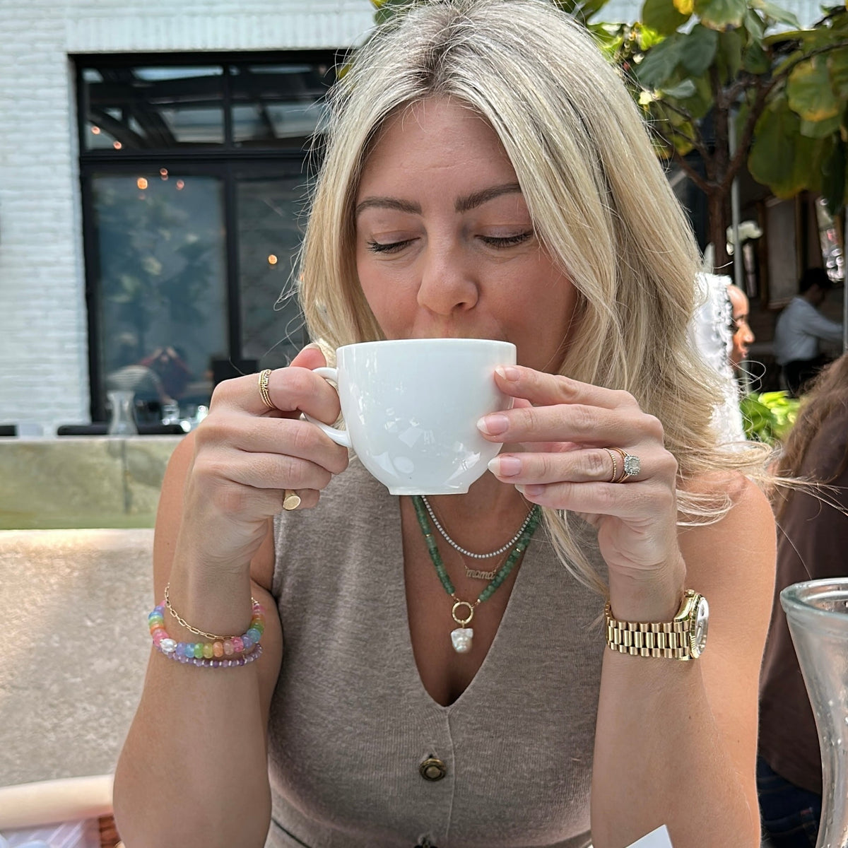 A blonde haired woman sipping a coffee in a white cup.