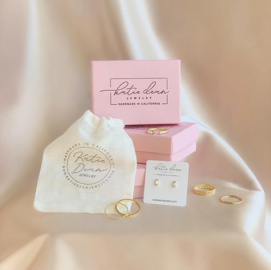 small pink boxes and canvas bag with hand stamped Katie Dean Jewelry logo and dainty earrings and stacking rings