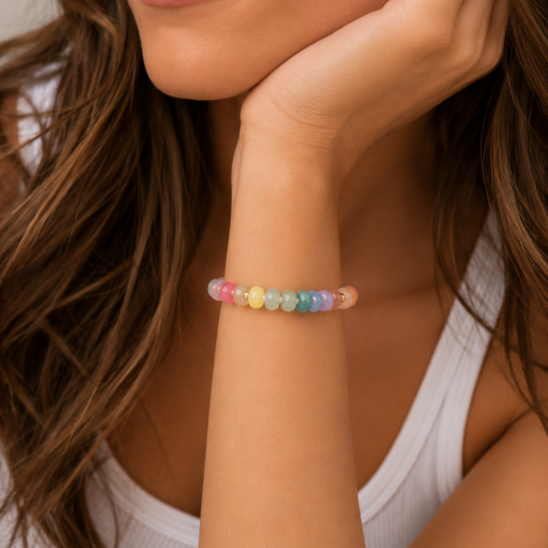 A close-up of a woman wearing a beaded bracelet on her wrist. The bracelet features small, round beads in pastel rainbow colors including pink, orange, yellow, green, blue, and purple.