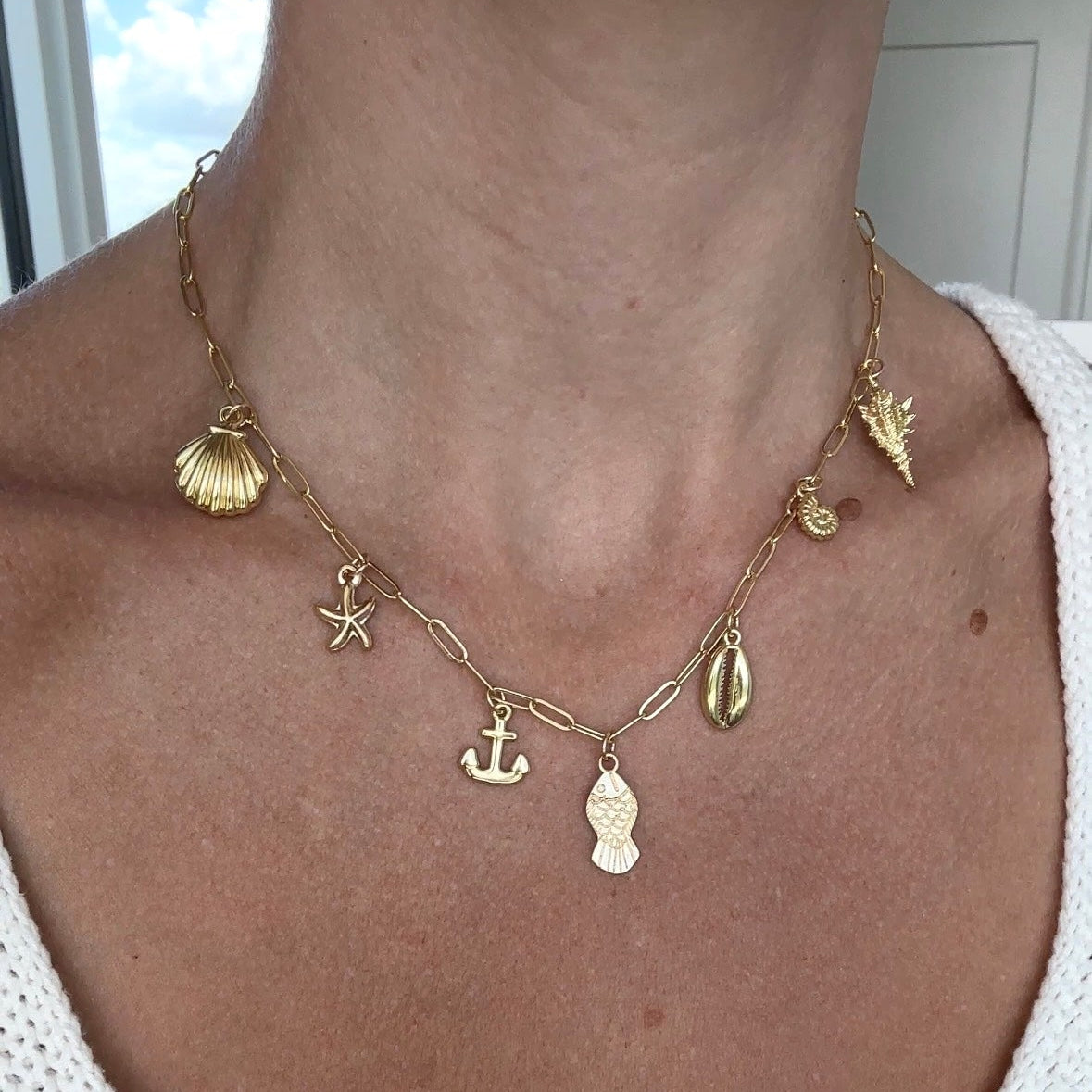 Gold necklace with various charms worn by a person in a white top.