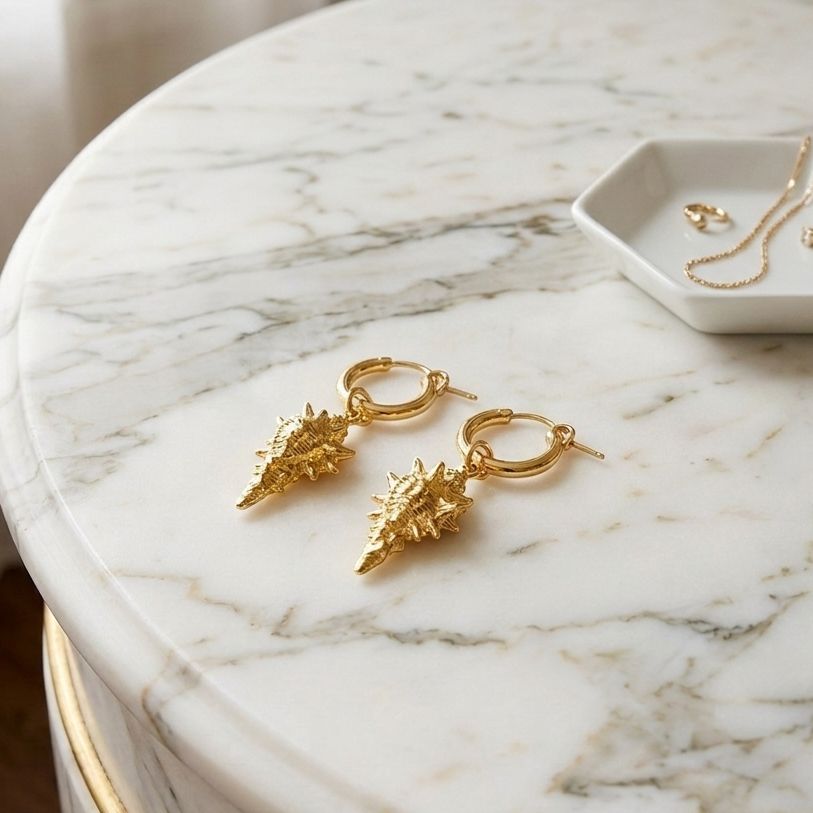gold hoop earrings with detailed conch shell charms on a marble vanity