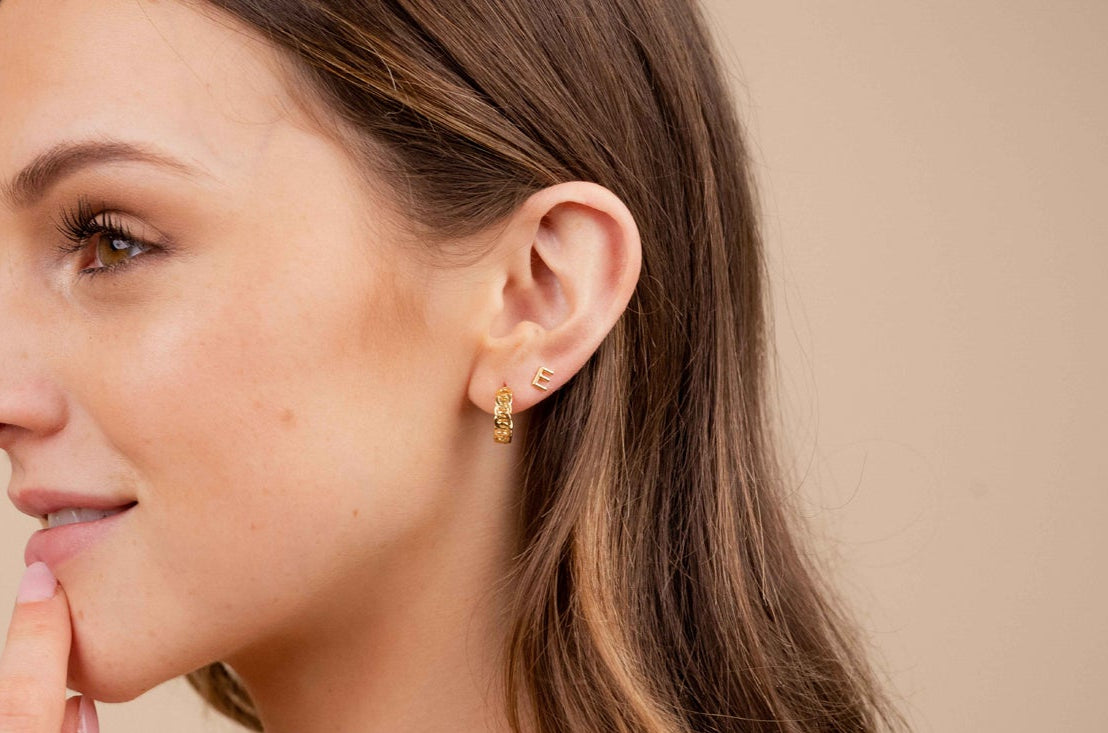 Woman wearing gold earrings and a ring on a beige background