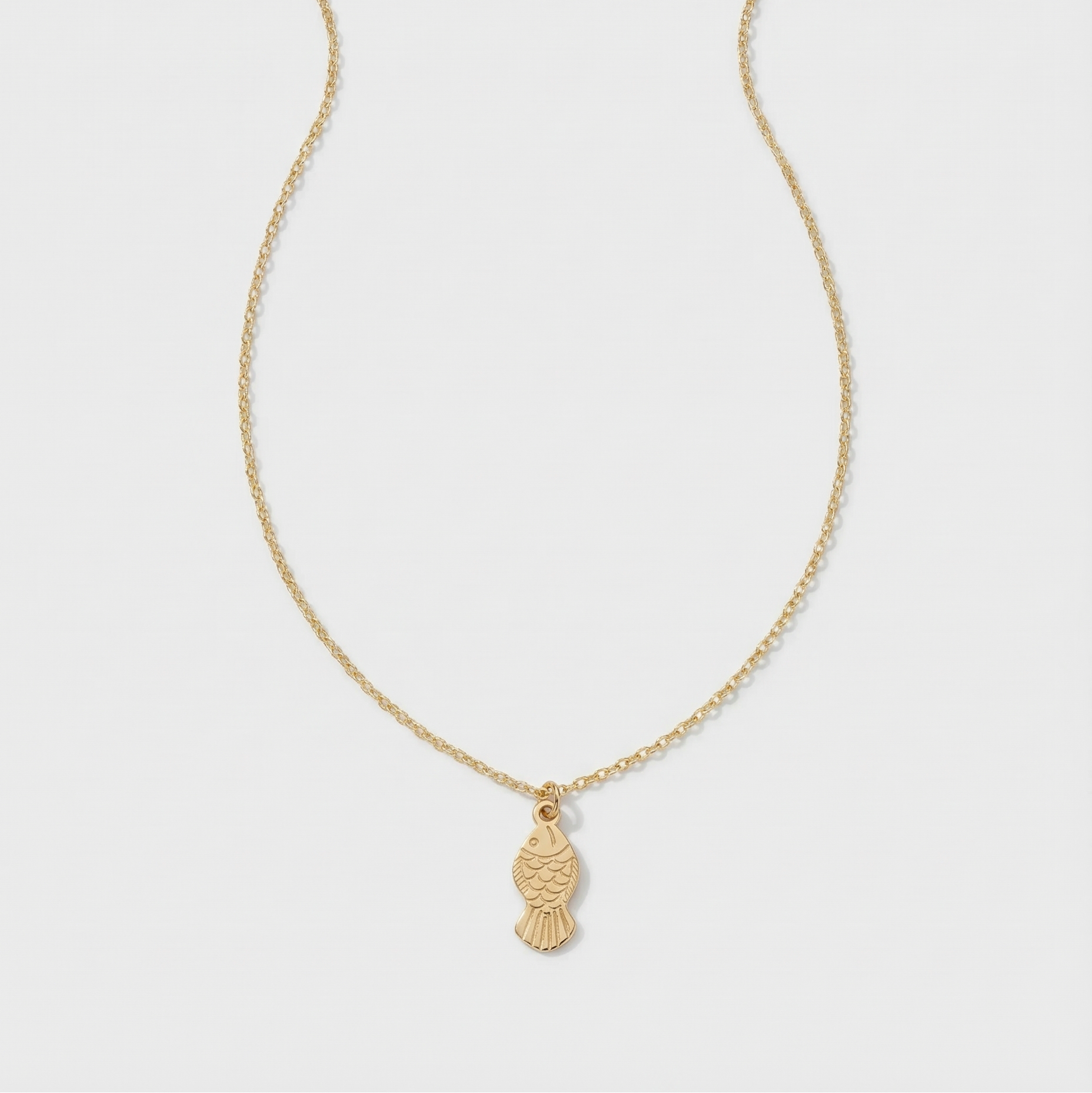 Gold necklace with a fish pendant on a light gray background