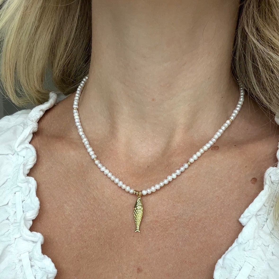 Pearl necklace with a gold pendant worn by a person in a white blouse.