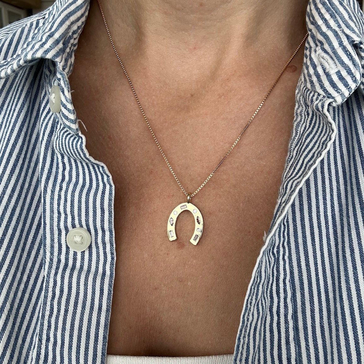 Person wearing a gold horseshoe necklace with a striped button down shirt dainty gold necklace made by Katie Dean Jewelry.