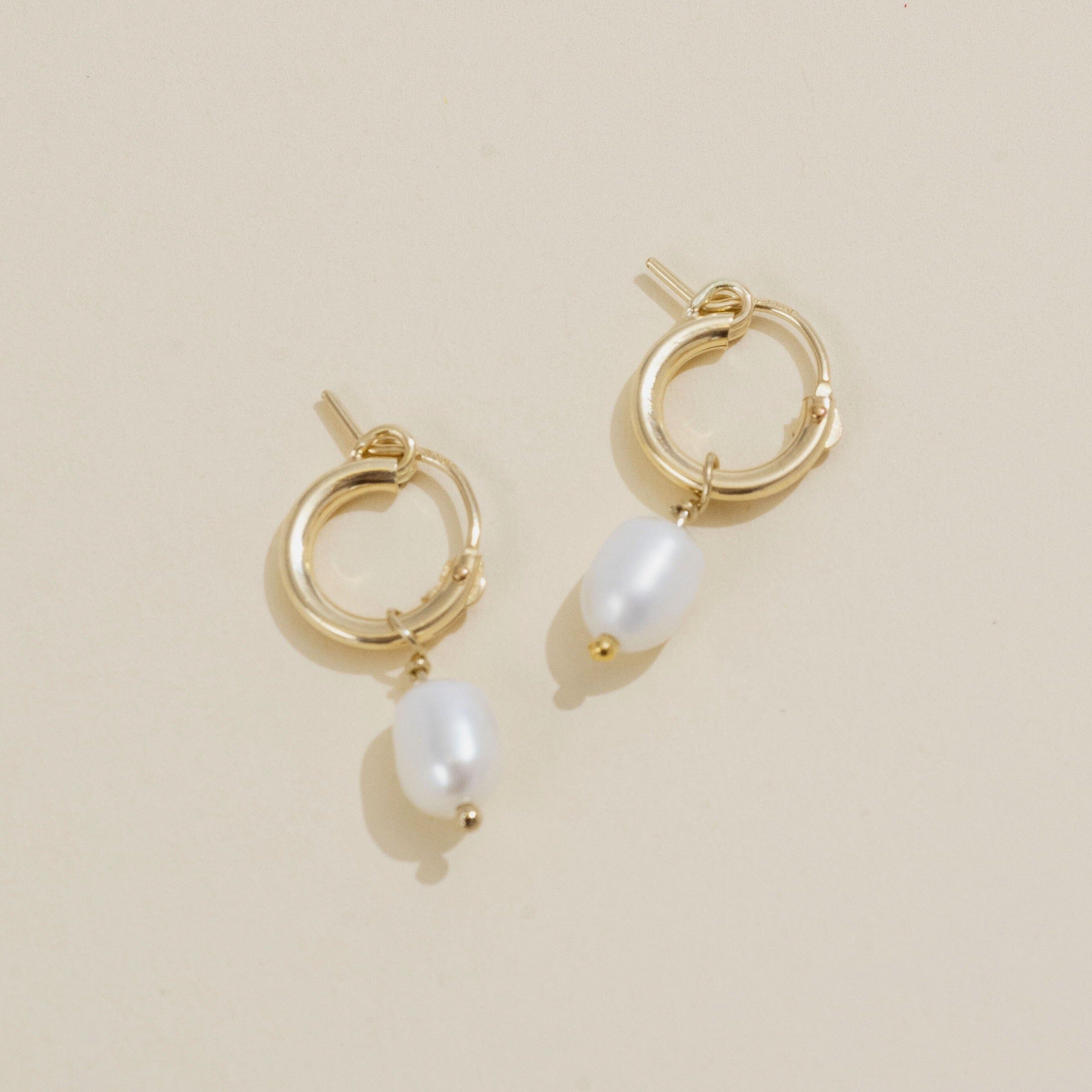Dainty gold Pearl hoops by Katie Dean Jewelry as seen on a tan background.
