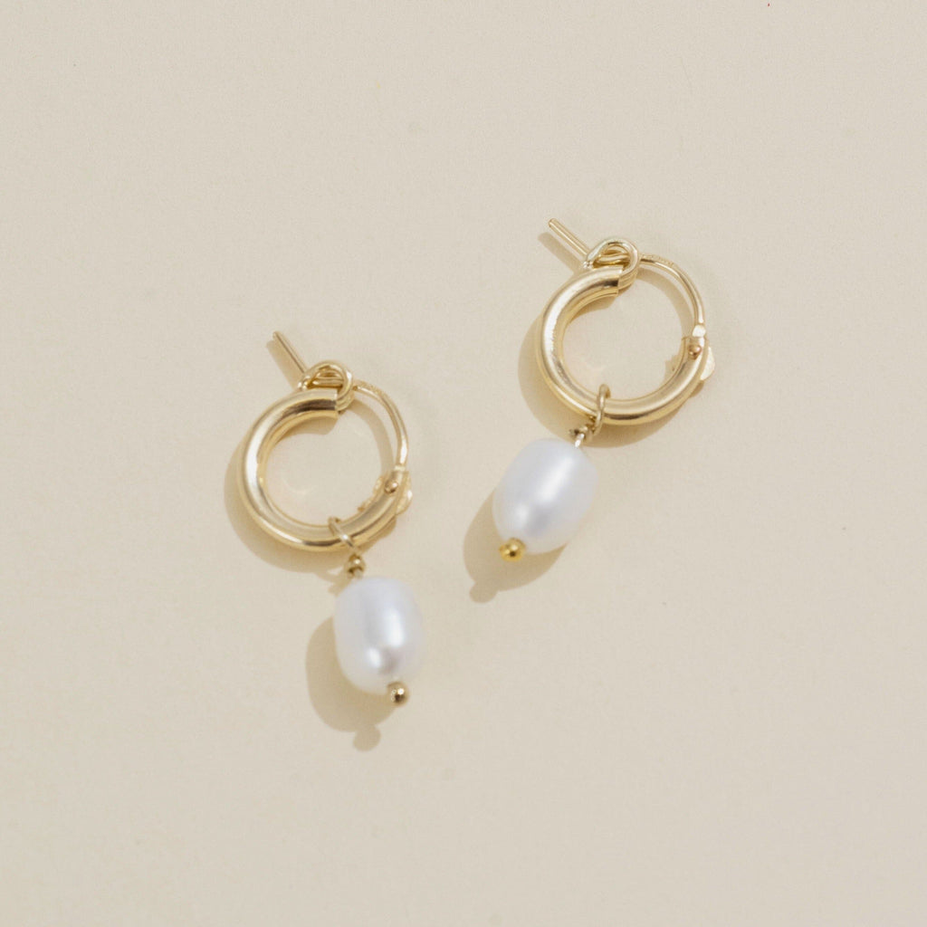 Dainty gold Pearl hoops by Katie Dean Jewelry as seen on a tan background.