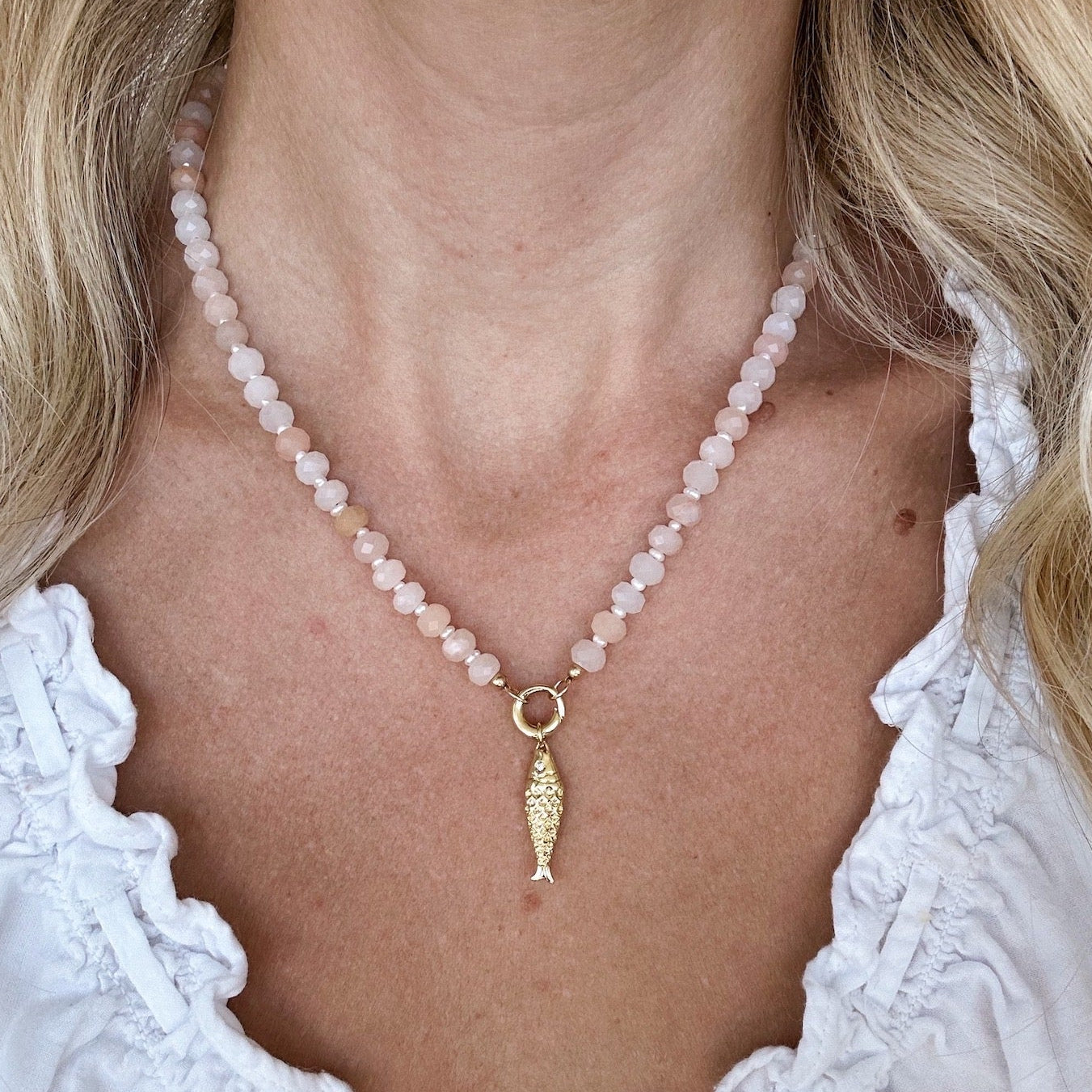 Necklace with pink aventurine beads and a gold fish charm on a white background handmade by Katie Dean Jewelry worn by a person with a white top.
